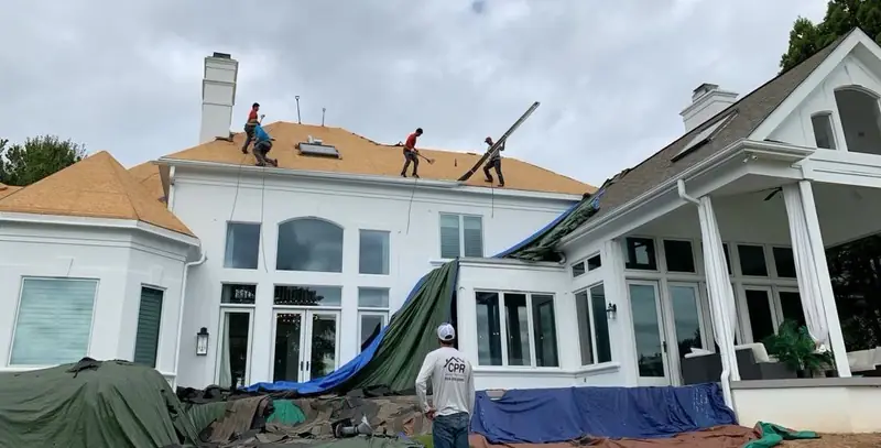 Crew replacing the roof on a white home with large windows, tarps over the patio